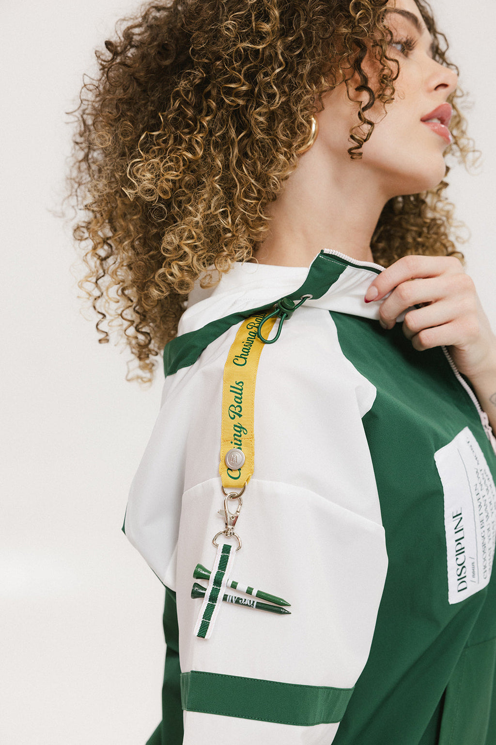 A woman wearing a green and white hoodie with a half-zip design, kangaroo pocket, and decorative woven ribbons.