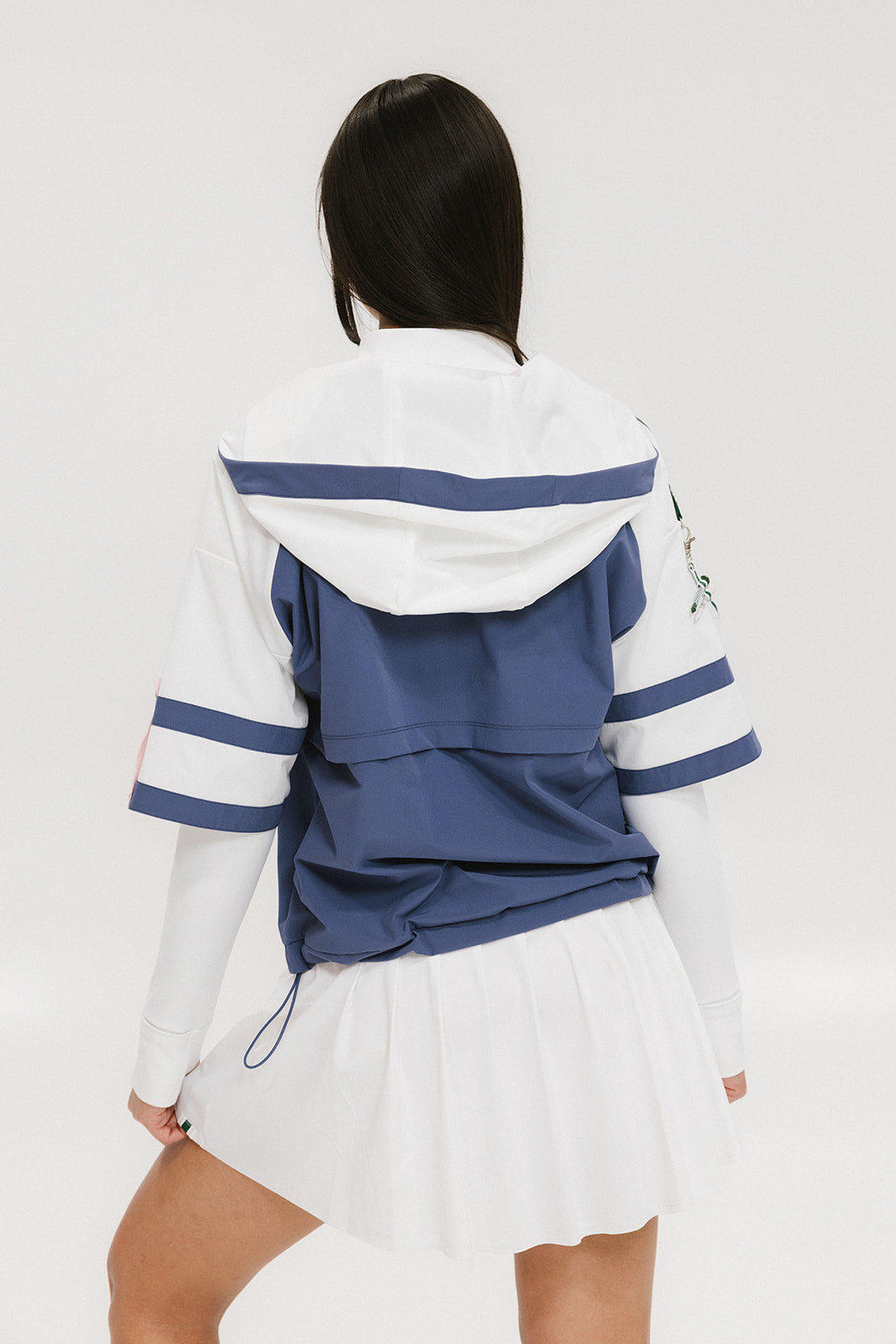 A woman wearing a blue and white hoodie with a half-zip feature and a kangaroo pocket, paired with a white skirt.