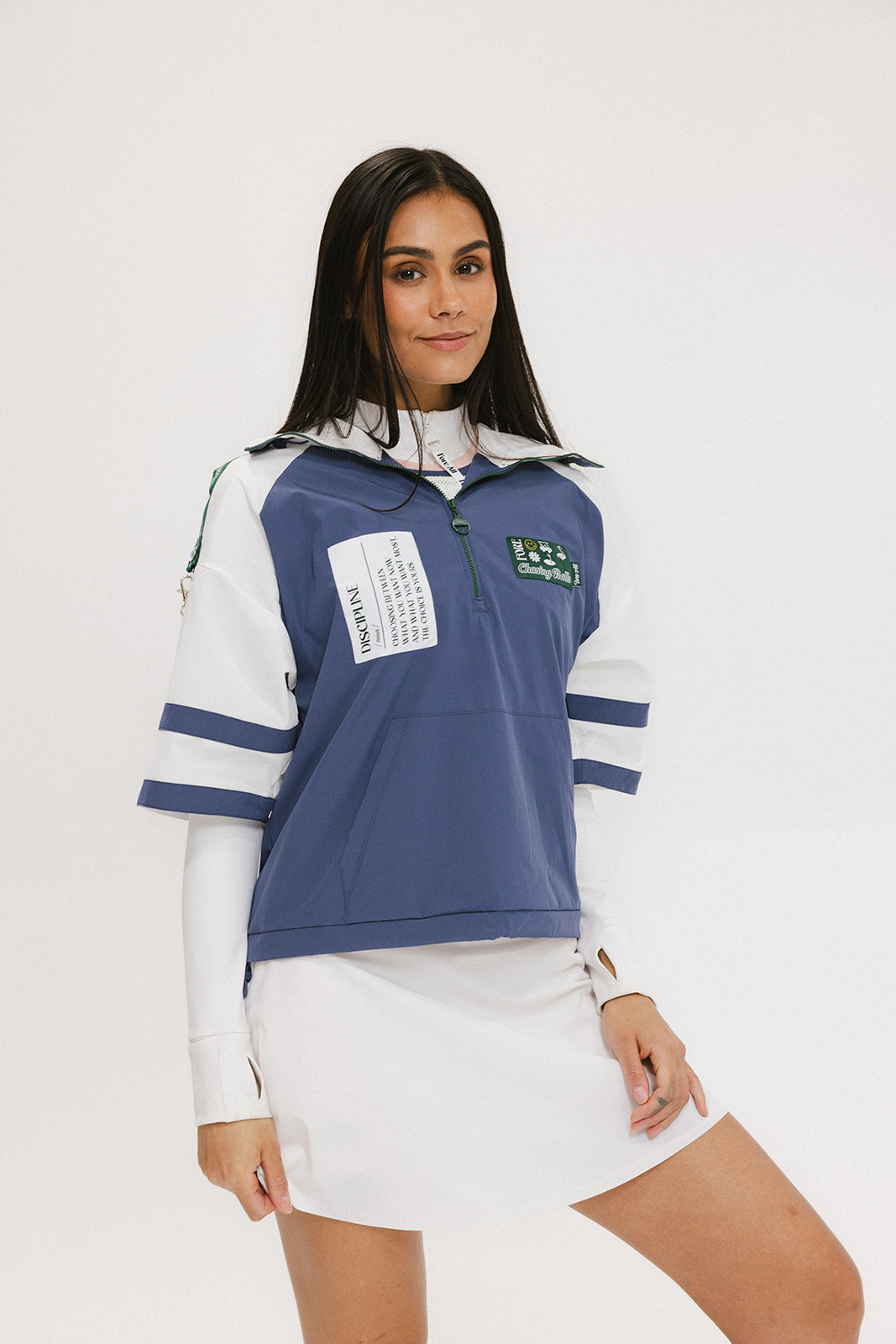 A woman wearing a blue and white hoodie with a half-zip feature and a kangaroo pocket, paired with a white skirt.