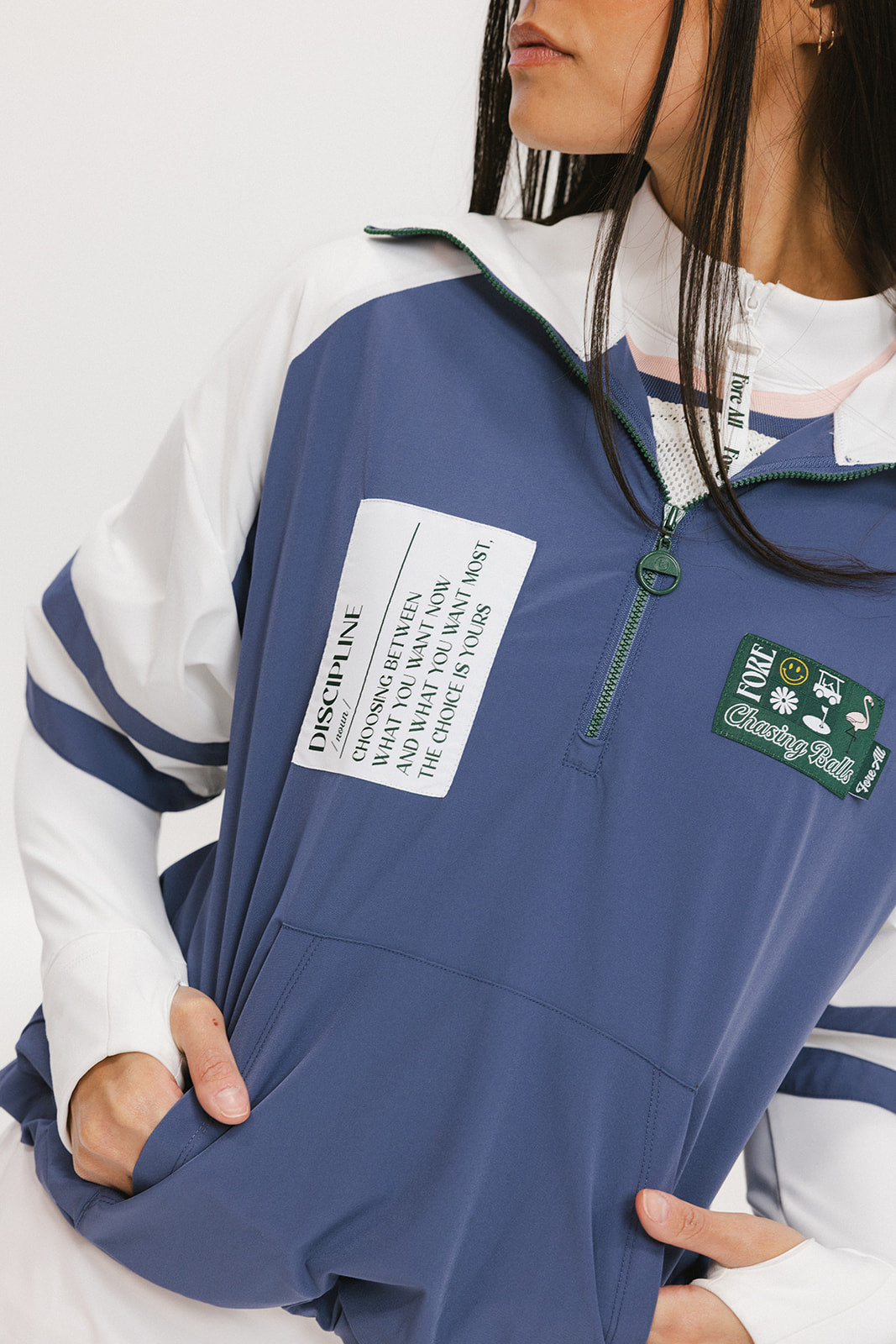 A woman wearing a blue and white hoodie with a half-zip feature and a kangaroo pocket, paired with a white skirt.