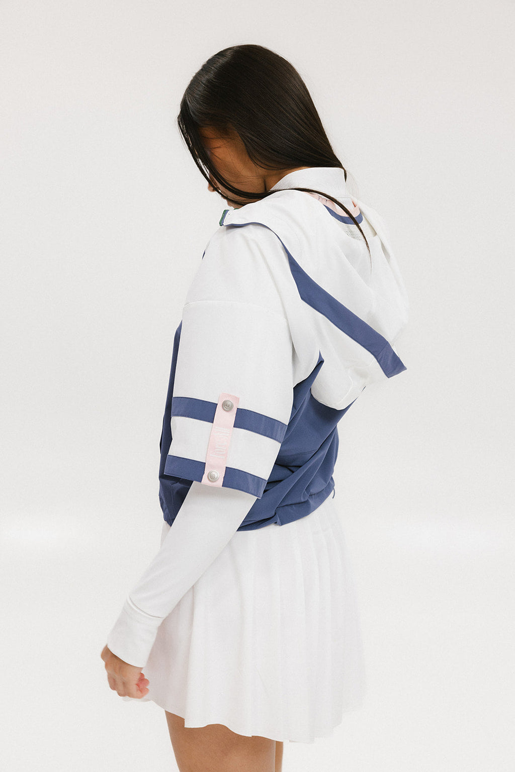 A woman wearing a blue and white hoodie with a half-zip feature and a kangaroo pocket, paired with a white skirt.