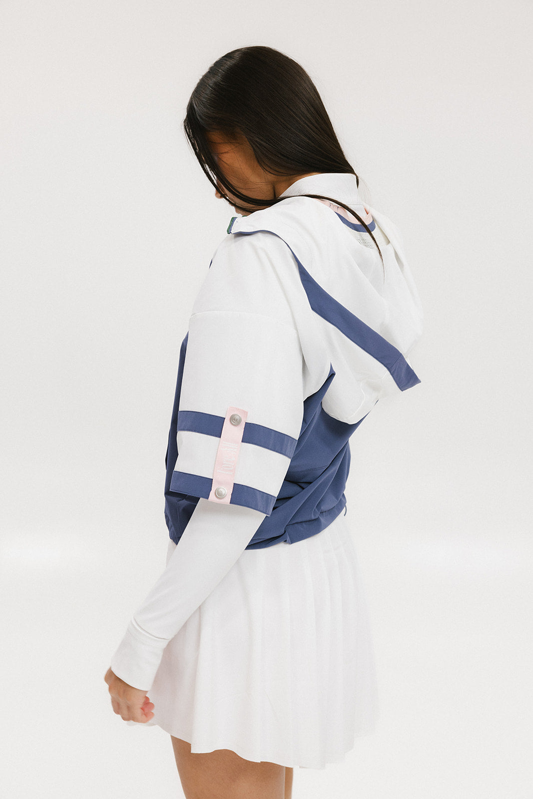 A woman wearing a blue and white hoodie with a half-zip feature and a kangaroo pocket, paired with a white skirt.