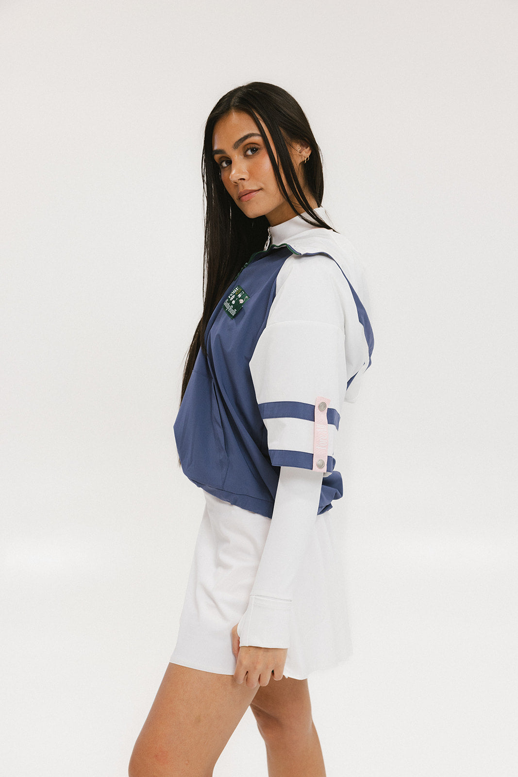 A woman wearing a blue and white hoodie with a half-zip feature and a kangaroo pocket, paired with a white skirt.