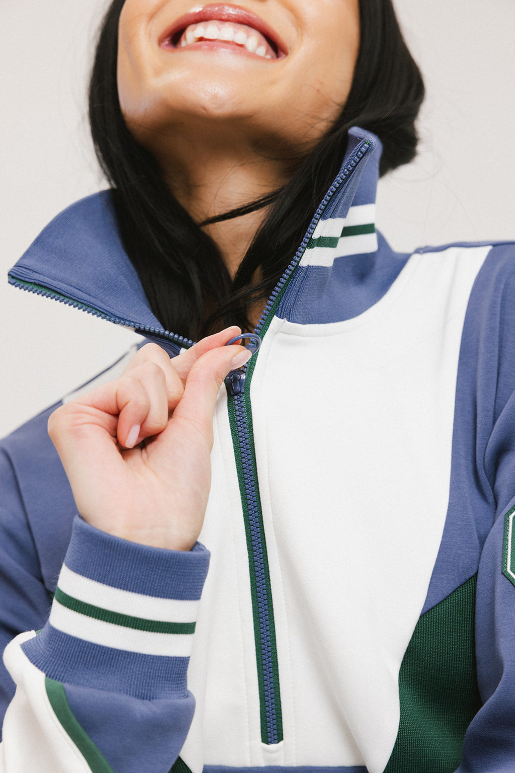 A woman wearing a half zip sports top with colorblocking in blue, white, and green, and ribbed detailing around the collar, cuffs, and hem.