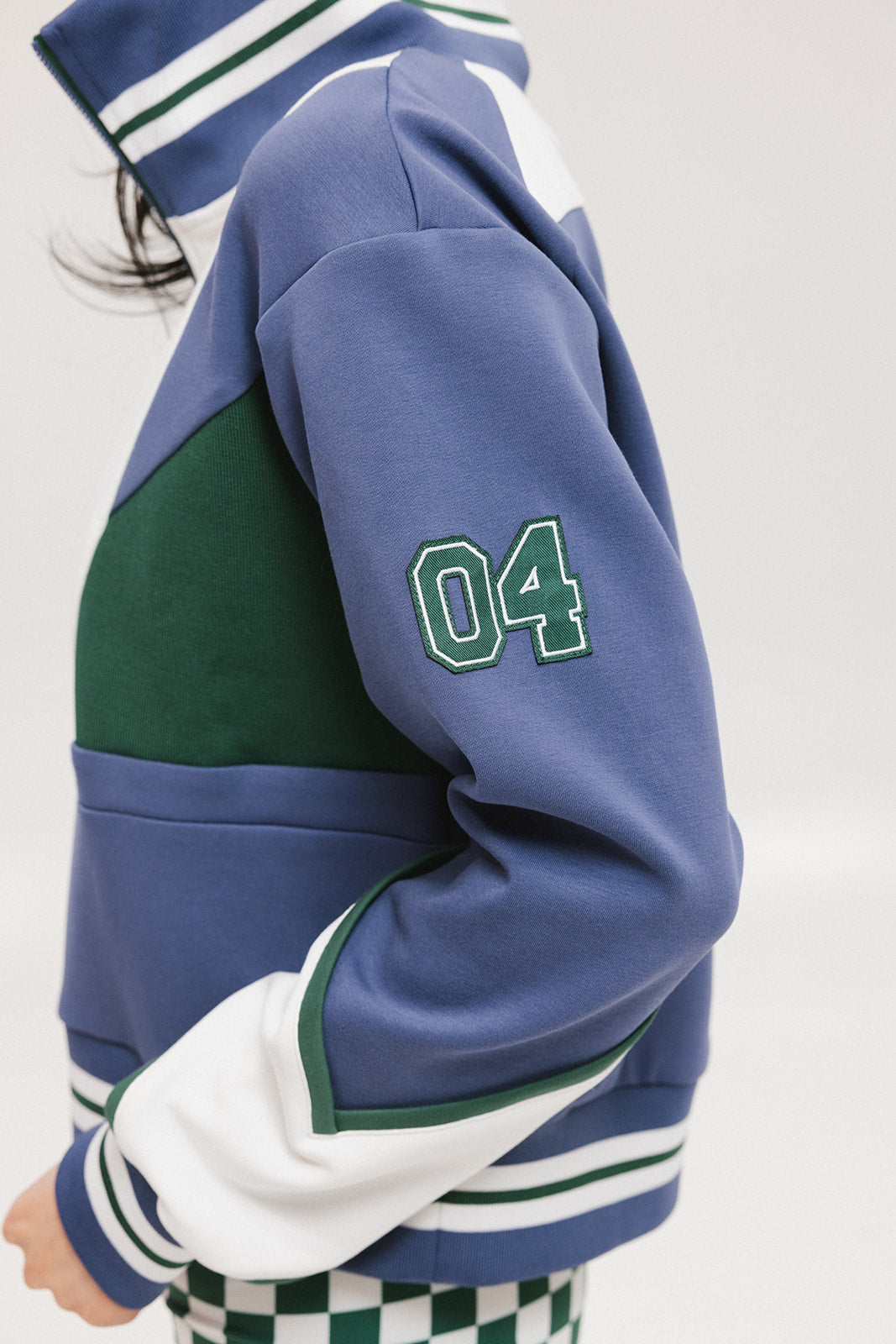 A woman wearing a half zip sports top with colorblocking in blue, white, and green, and ribbed detailing around the collar, cuffs, and hem.