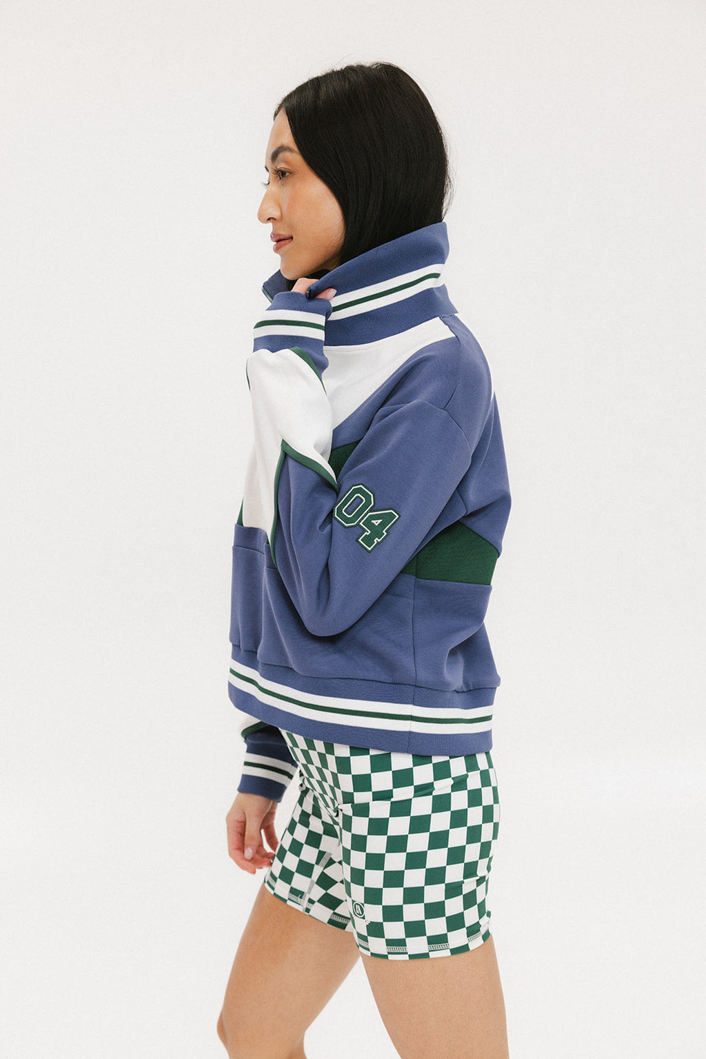 A person wearing a blue and white striped half zip top with long sleeves and a high collar, paired with checkered green and white shorts.