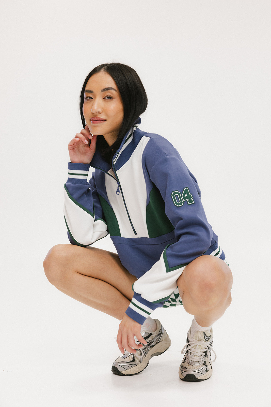 A woman wearing a half zip sports top with colorblocking in blue, white, and green, and ribbed detailing around the collar, cuffs, and hem.