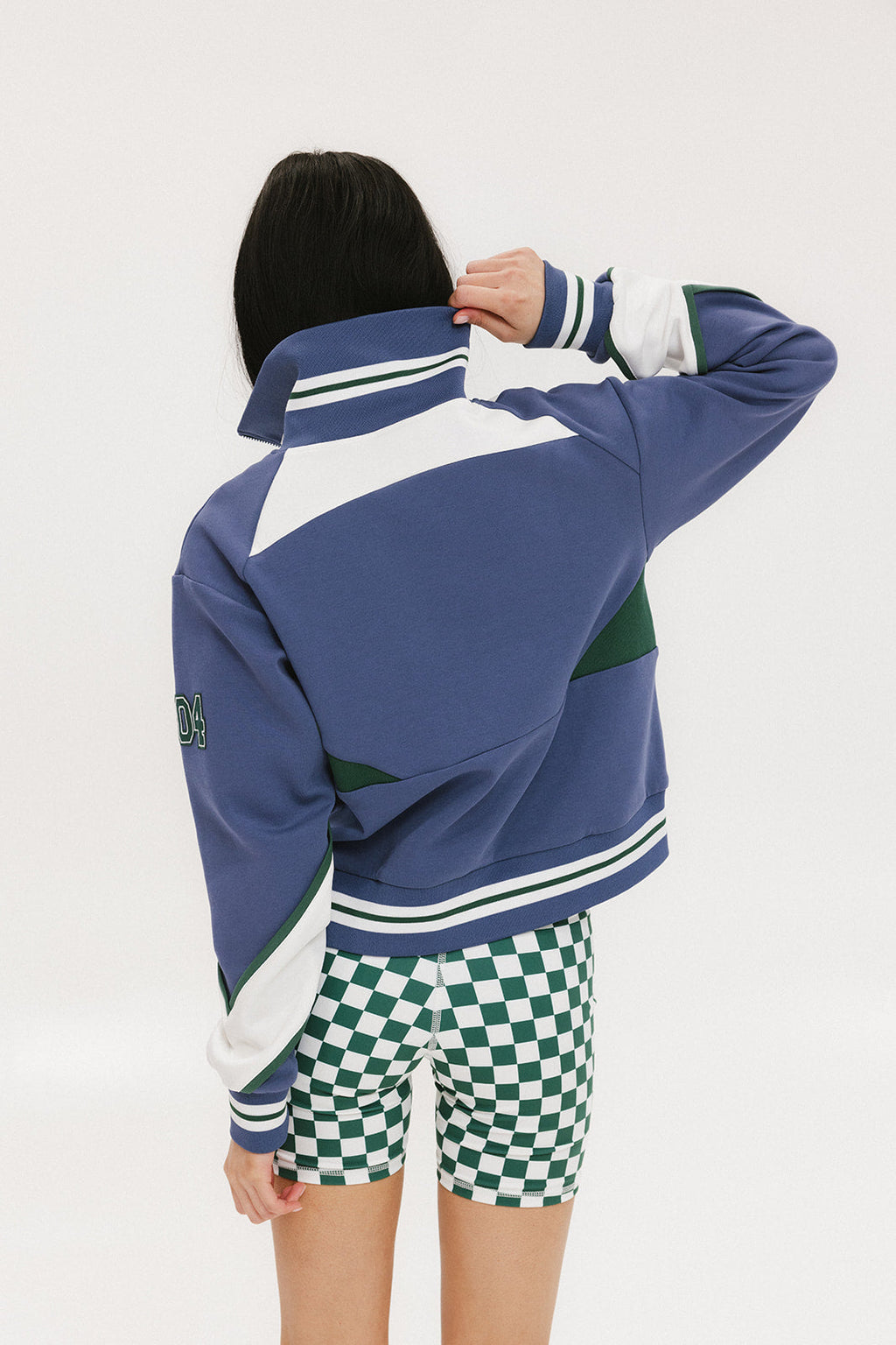 A woman wearing a half zip sports top with colorblocking in blue, white, and green, and ribbed detailing around the collar, cuffs, and hem.