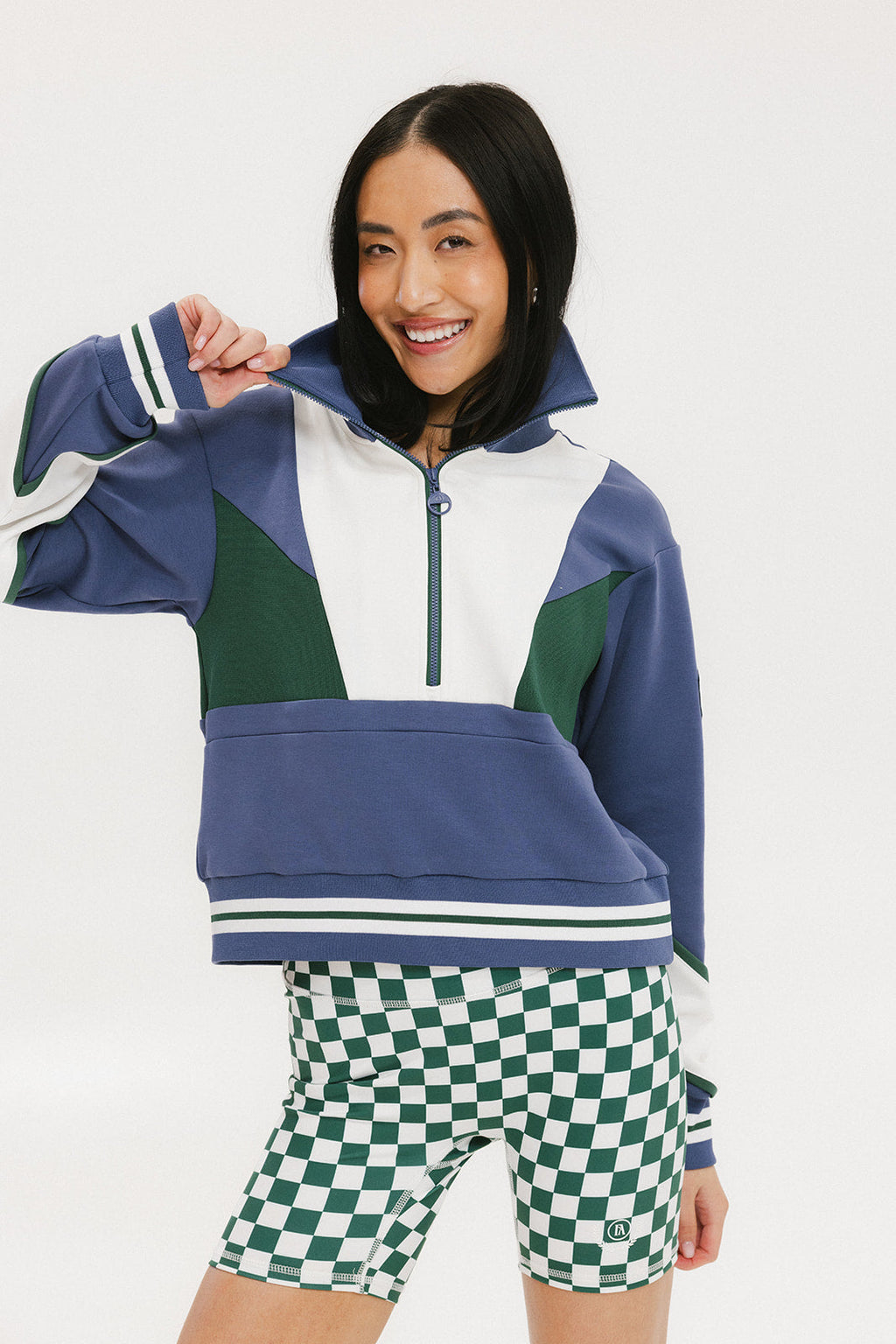 A woman wearing a half zip sports top with colorblocking in blue, white, and green, and ribbed detailing around the collar, cuffs, and hem.