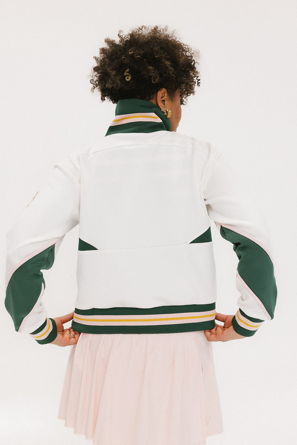 A woman wearing a white half zip sports top with green color blocking and ribbed detailing around the collar, cuffs, and hem. The top features half sleeve design with a signature logo on the chest.