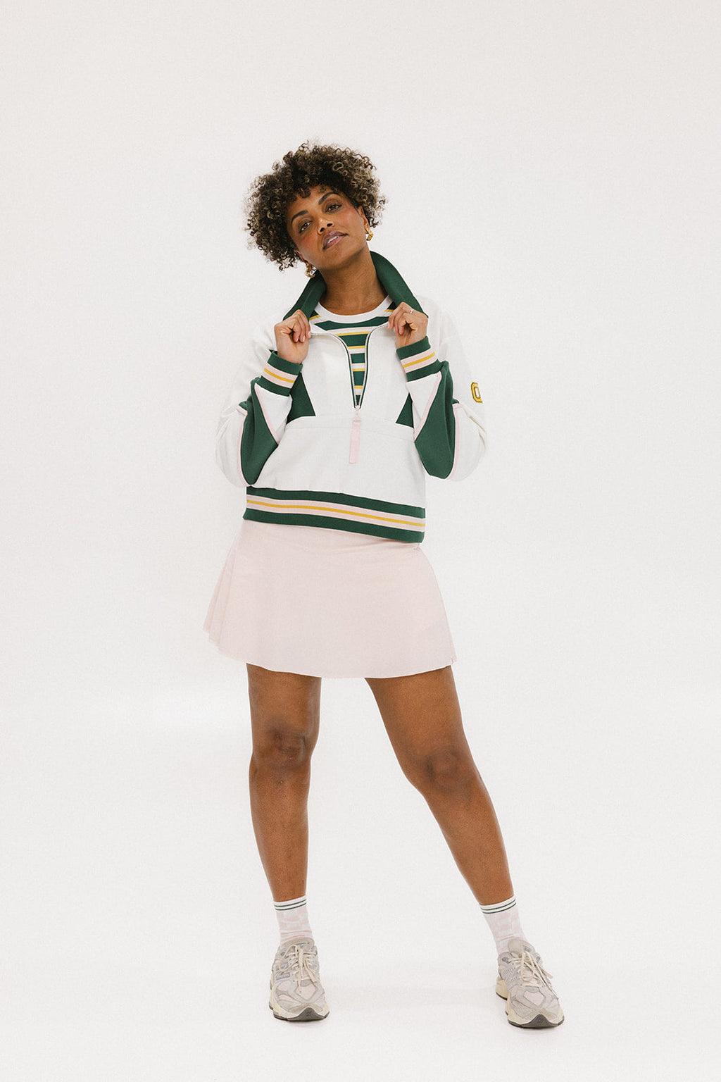 A woman wearing a white half zip sports top with green color blocking and ribbed detailing around the collar, cuffs, and hem. The top features half sleeve design with a signature logo on the chest.