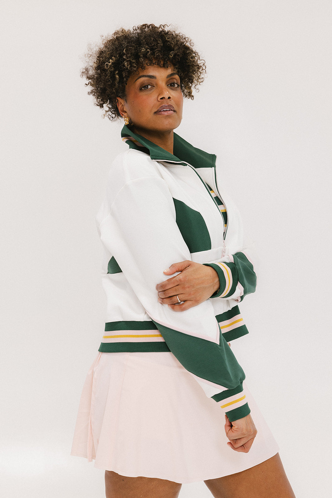 A woman wearing a white half zip sports top with green color blocking and ribbed detailing around the collar, cuffs, and hem. The top features half sleeve design with a signature logo on the chest.
