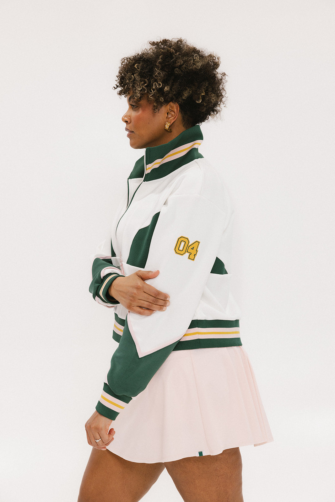 A woman wearing a white half zip sports top with green color blocking and ribbed detailing around the collar, cuffs, and hem. The top features half sleeve design with a signature logo on the chest.