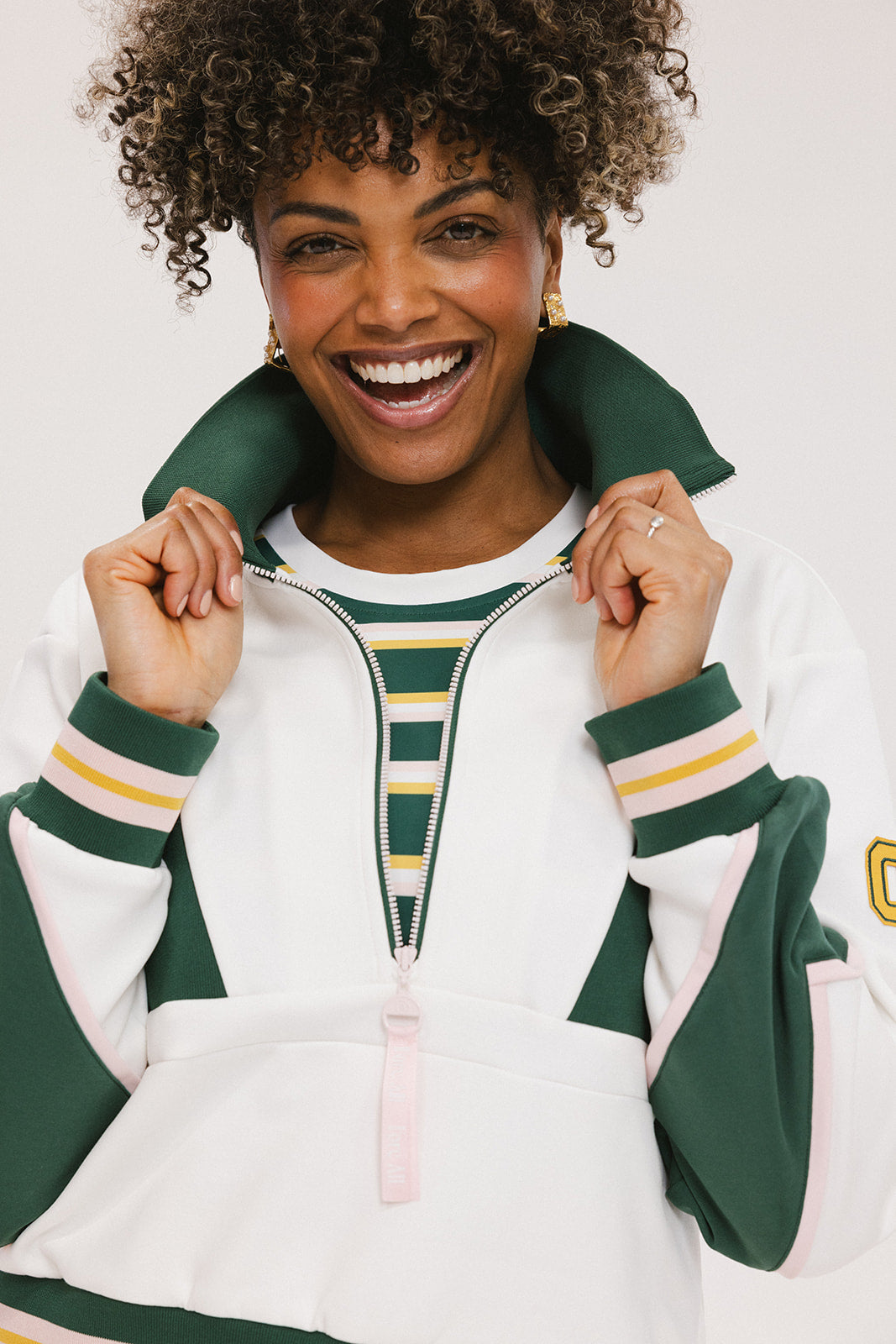 A woman wearing a white half zip sports top with green color blocking and ribbed detailing around the collar, cuffs, and hem. The top features half sleeve design with a signature logo on the chest.