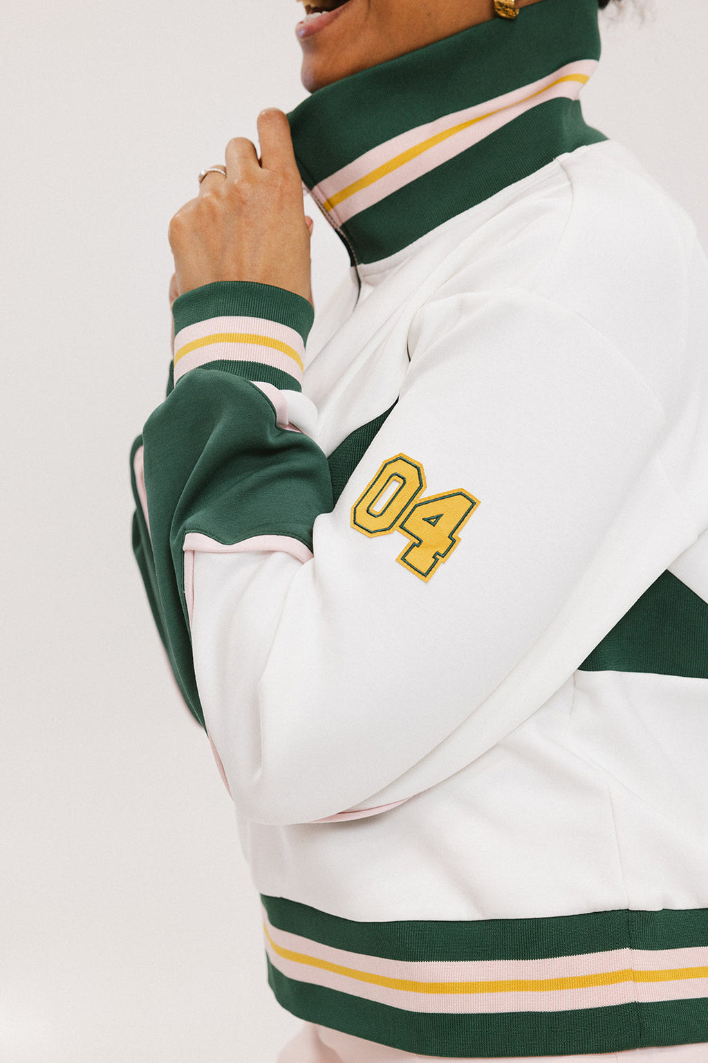 A woman wearing a white half zip sports top with green color blocking and ribbed detailing around the collar, cuffs, and hem. The top features half sleeve design with a signature logo on the chest.