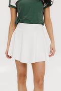 A person wearing a white skirt with a mesh back, paired with a green top and matching green and white sneakers. The skirt has a grippy elastic hem and built-in biddy shorties with pockets.