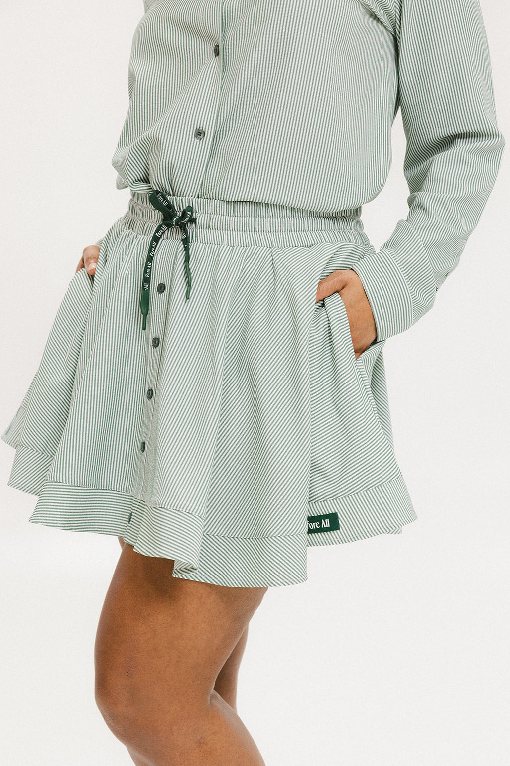 Model wearing the patty skirt in green seersucker. Featuring a green drawstring, buttons down the front, and a fore all logo on the bottom of the skirt.