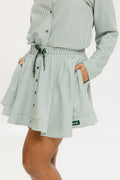 Model wearing the patty skirt in green seersucker. Featuring a green drawstring, buttons down the front, and a fore all logo on the bottom of the skirt.