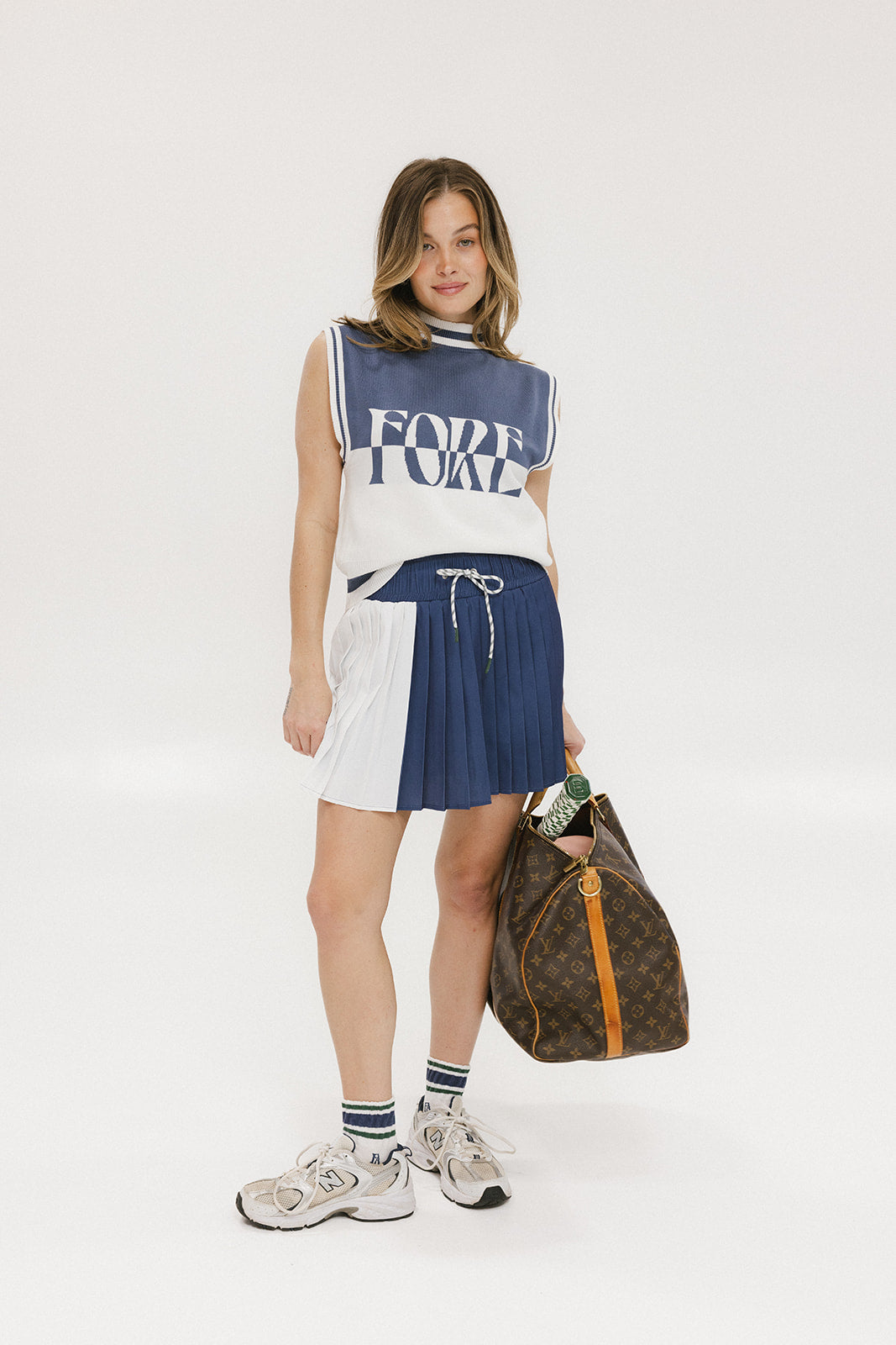 A pleated skirt with colorblocking in indigo and white, featuring a round drawstring cord at the waist and a 'Chasing Balls' icon patch on the back.