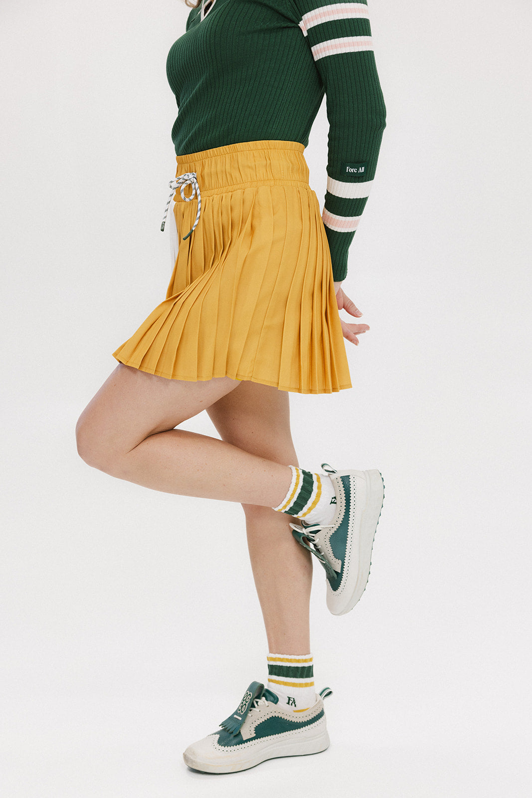 A person wearing a mustard pleated skirt with colorblocking, featuring a round drawstring cord.