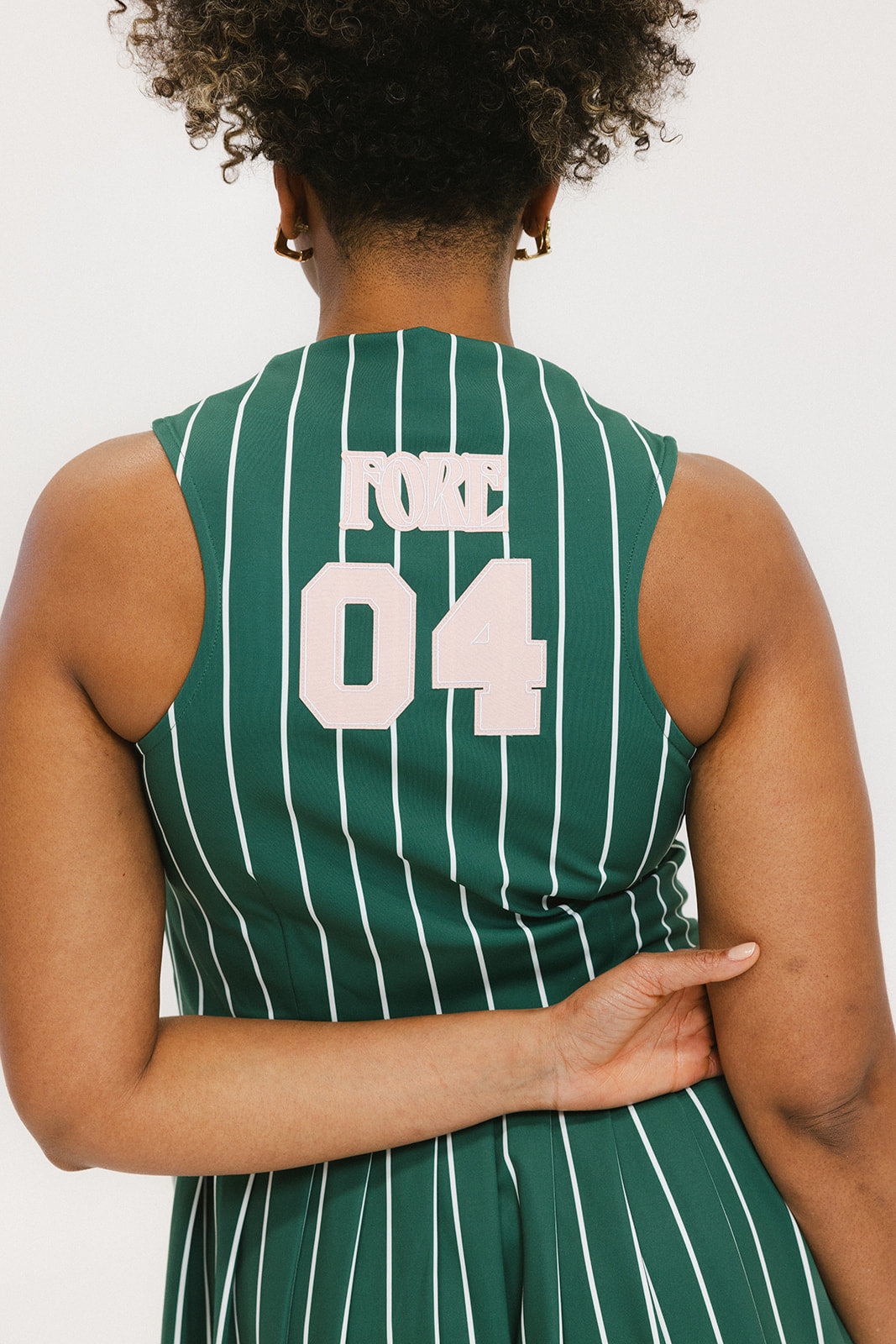 A woman wearing a sleeveless, pinstripe green dress with a pleated skirt, white trim, and applique logos.