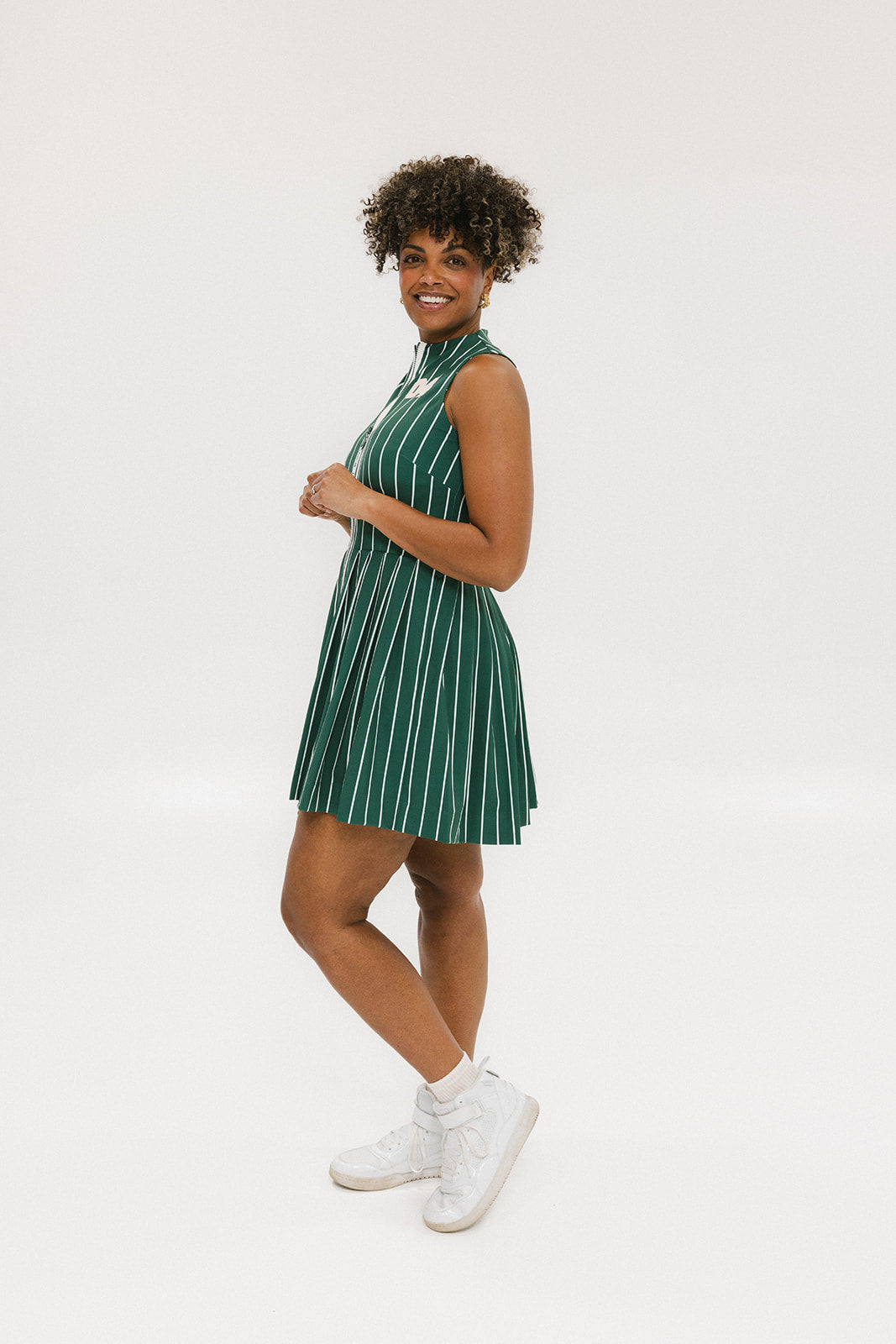 A woman wearing a sleeveless, pinstripe green dress with a pleated skirt, white trim, and applique logos.