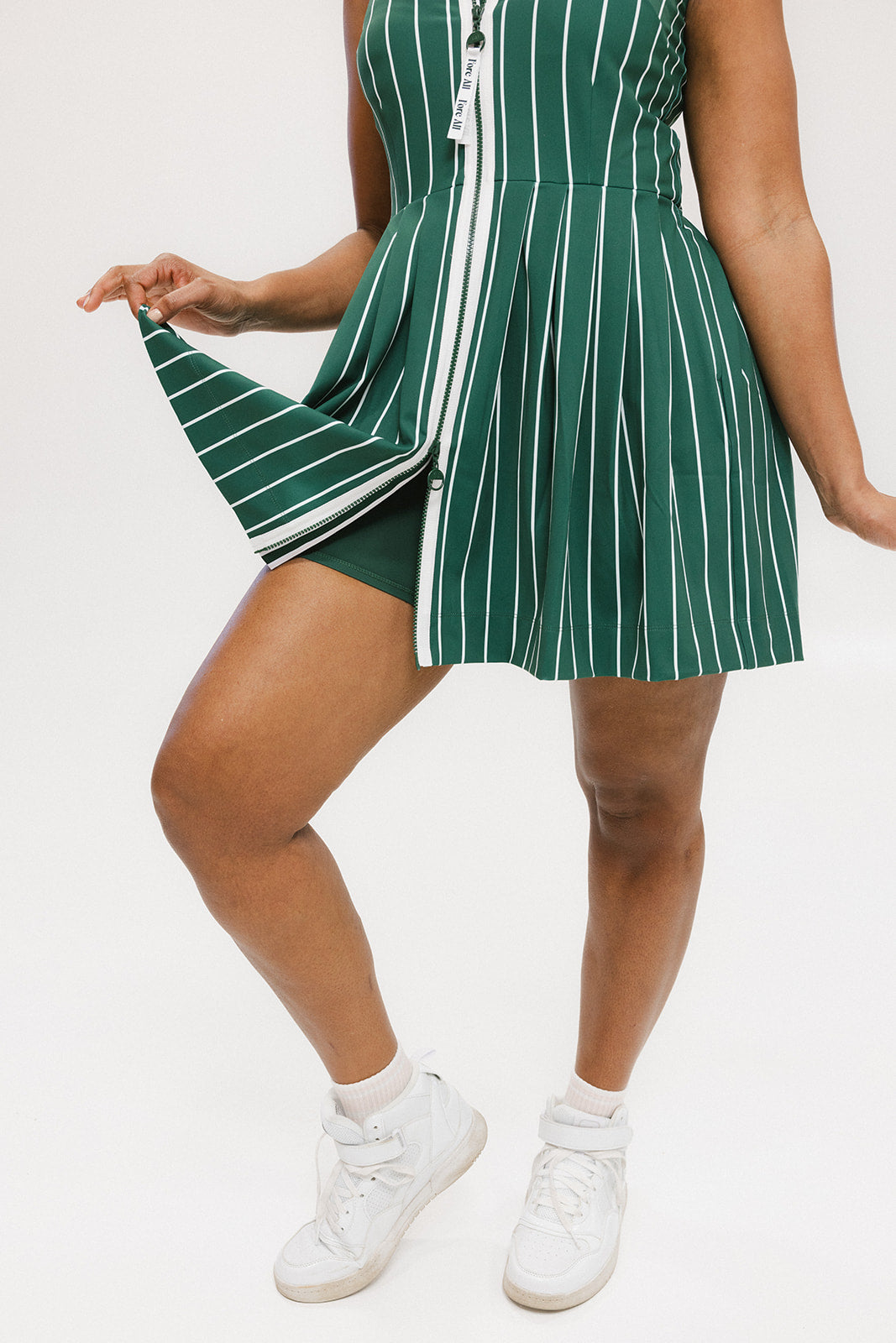 A woman wearing a sleeveless, pinstripe green dress with a pleated skirt, white trim, and applique logos.