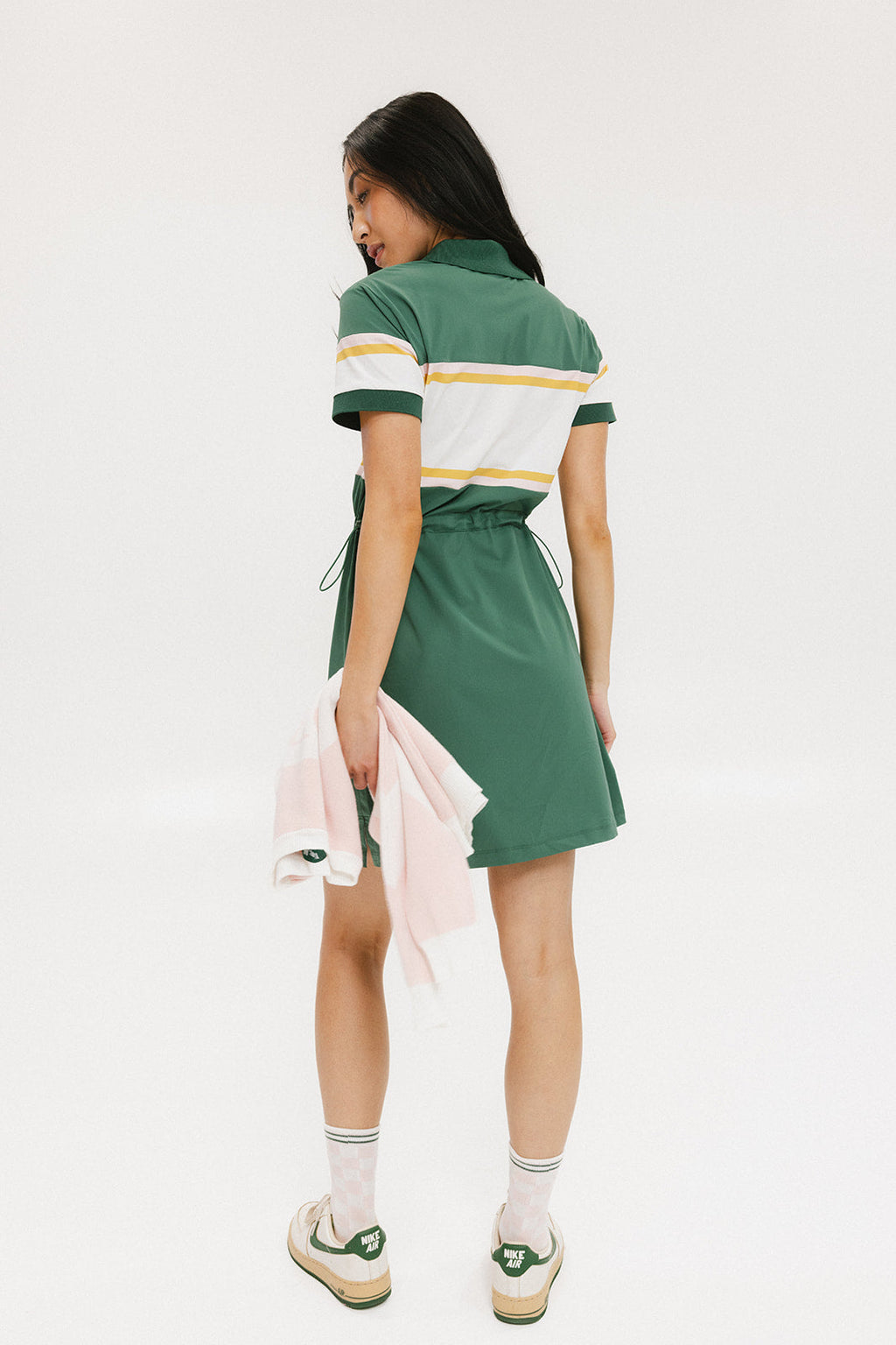 A person viewed from the back wearing a green dress with short sleeves and a round neckline. The dress has horizontal white and yellow stripes on the upper part.