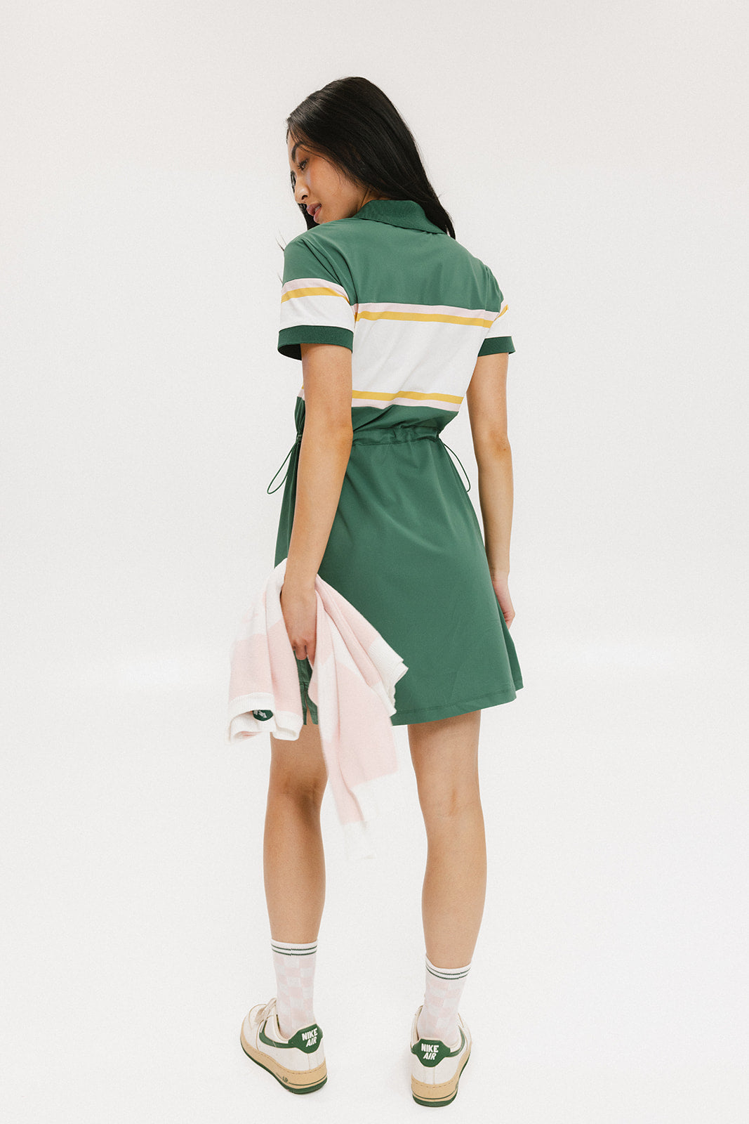 A person viewed from the back wearing a green dress with short sleeves and a round neckline. The dress has horizontal white and yellow stripes on the upper part.