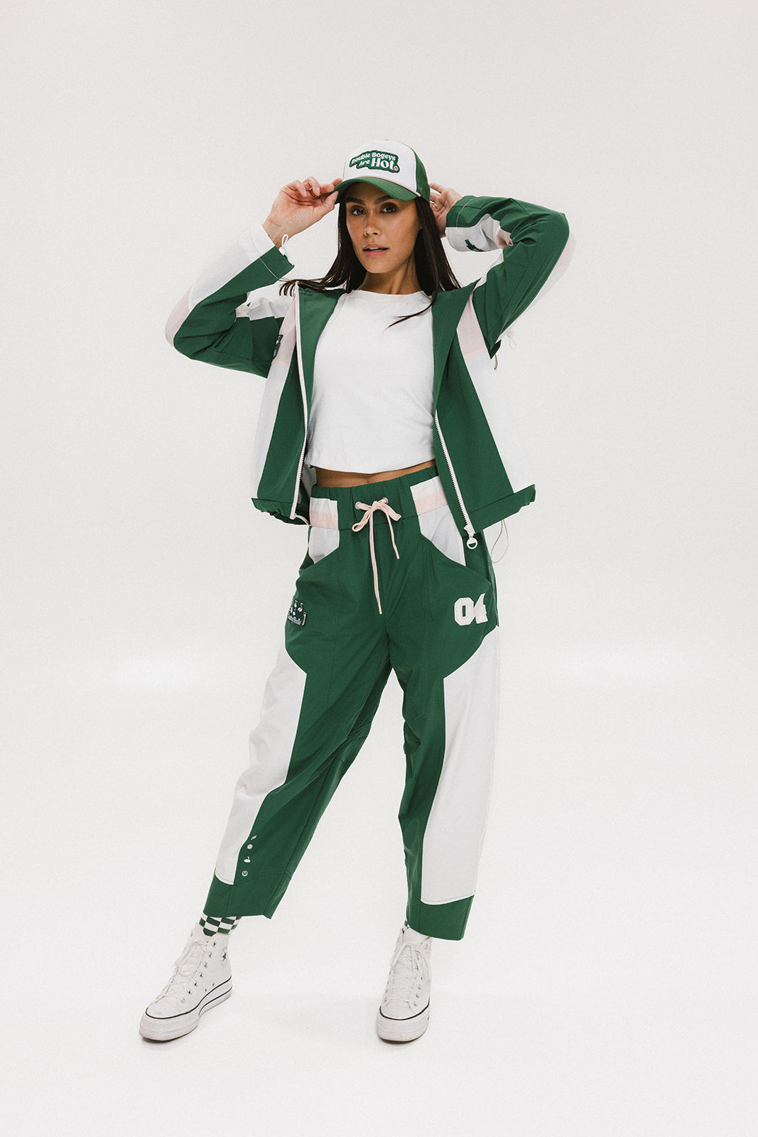 A pair of color-blocked green and white warm-up pants with a pink stripe, featuring a flat drawstring waistband and deep front pockets, branded with the 'Fore All' detail on the back and an FA icon on the inner calf.