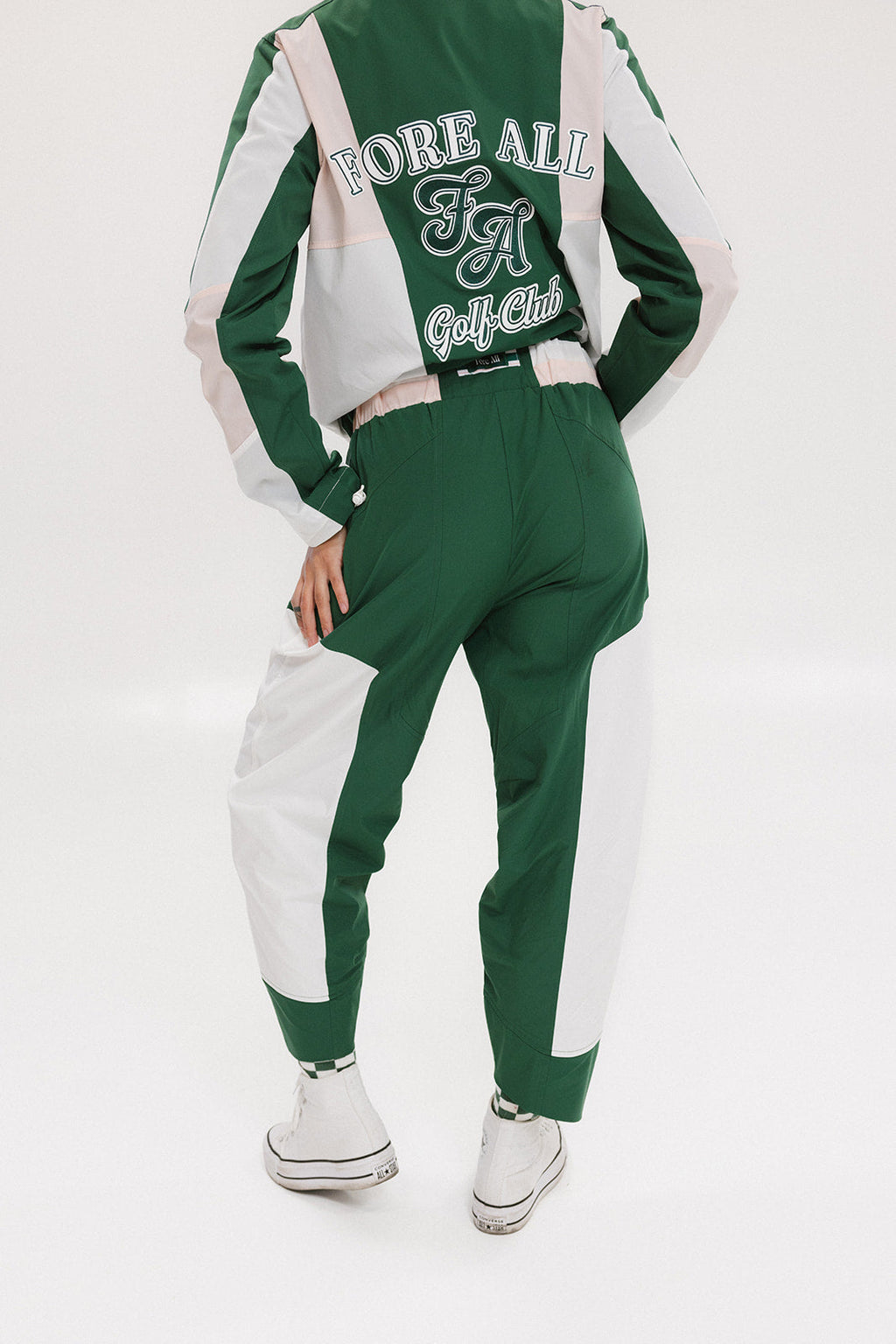 A pair of color-blocked green and white warm-up pants with a pink stripe, featuring a flat drawstring waistband and deep front pockets, branded with the 'Fore All' detail on the back and an FA icon on the inner calf.