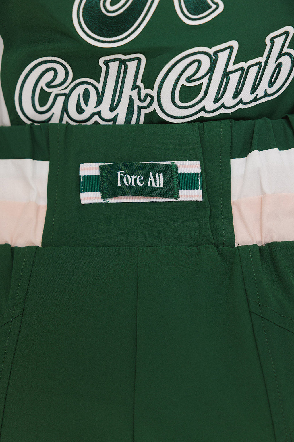 A pair of color-blocked green and white warm-up pants with a pink stripe, featuring a flat drawstring waistband and deep front pockets, branded with the 'Fore All' detail on the back and an FA icon on the inner calf.