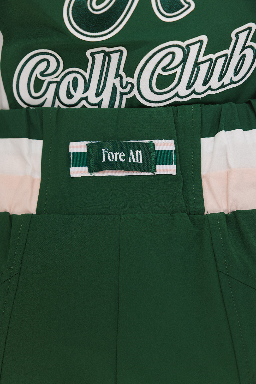 A pair of color-blocked green and white warm-up pants with a pink stripe, featuring a flat drawstring waistband and deep front pockets, branded with the 'Fore All' detail on the back and an FA icon on the inner calf.
