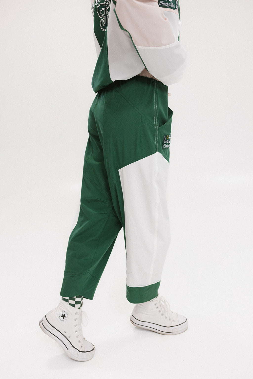 A pair of color-blocked green and white warm-up pants with a pink stripe, featuring a flat drawstring waistband and deep front pockets, branded with the 'Fore All' detail on the back and an FA icon on the inner calf.