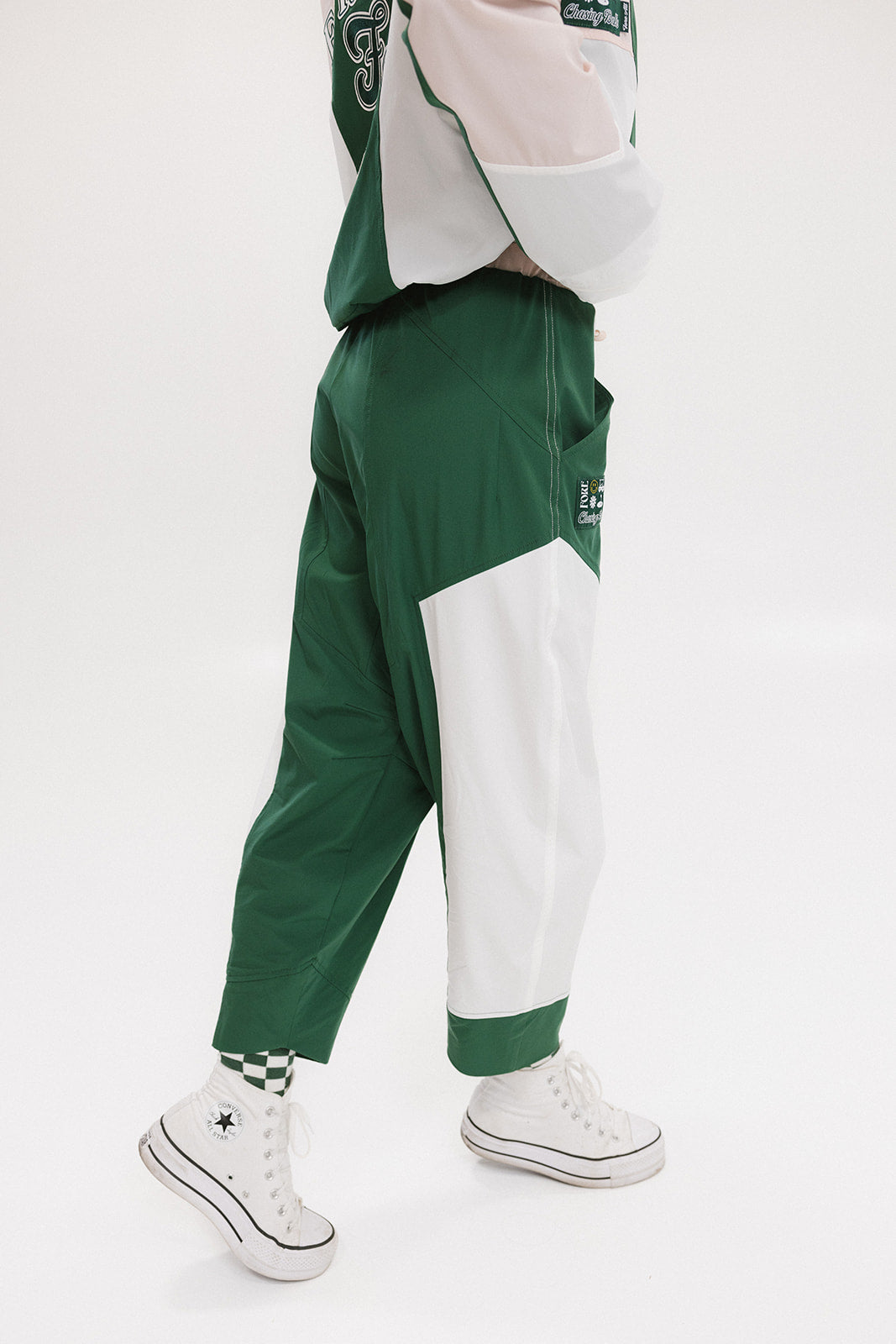 A pair of color-blocked green and white warm-up pants with a pink stripe, featuring a flat drawstring waistband and deep front pockets, branded with the 'Fore All' detail on the back and an FA icon on the inner calf.