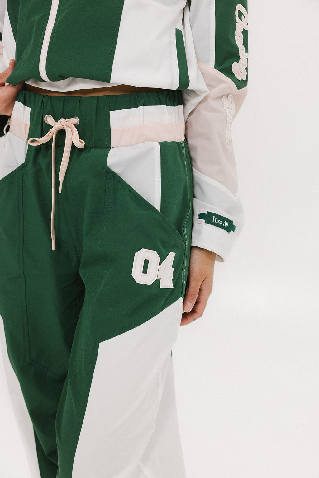 A pair of Caitlin Warm-Up Pants in green, pink, and white colors, featuring a drawstring waist and number '04' on the leg.