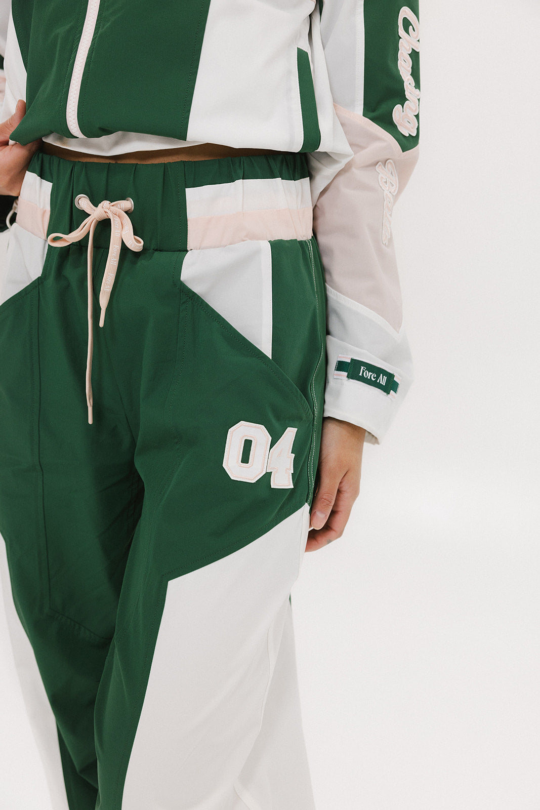 A pair of Caitlin Warm-Up Pants in green, pink, and white colors, featuring a drawstring waist and number '04' on the leg.