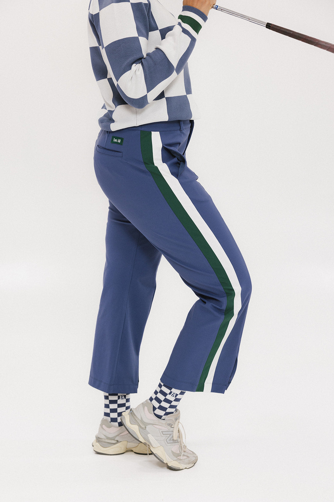 A person wearing the Simone Pant in blue with white stripes on the side, featuring princess seams down the leg and a slit at the hem. The person is also wearing a checkered blue and white top and white sneakers.