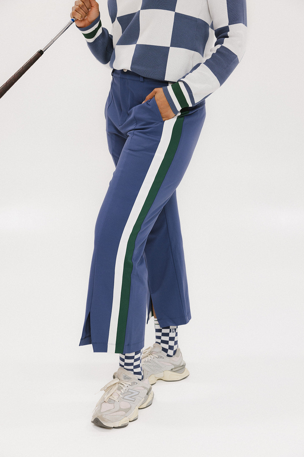 A person wearing the Simone Pant in blue with white stripes on the side, featuring princess seams down the leg and a slit at the hem. The person is also wearing a checkered blue and white top and white sneakers.