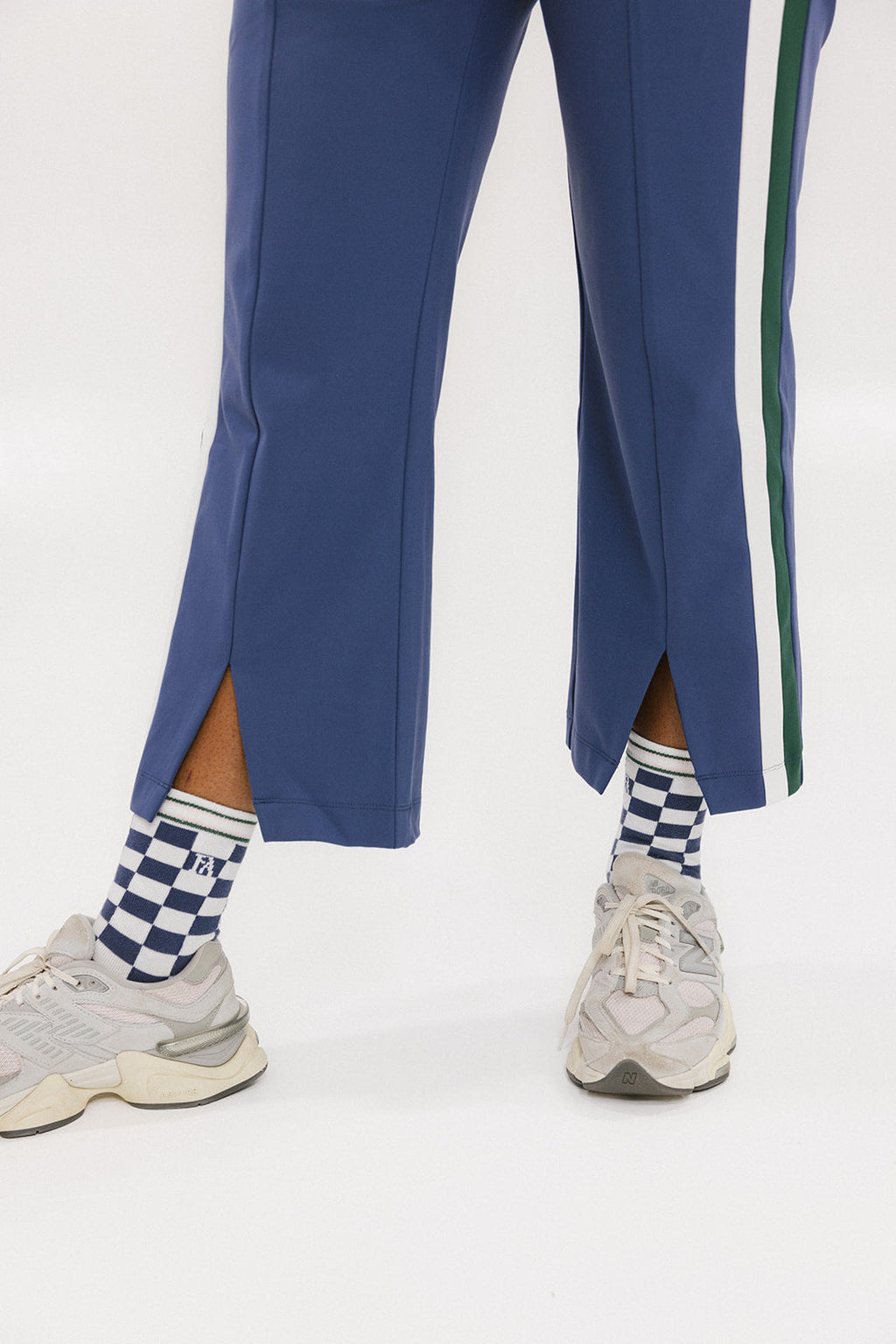 A person wearing the Simone Pant in blue with white stripes on the side, featuring princess seams down the leg and a slit at the hem. The person is also wearing a checkered blue and white top and white sneakers.