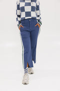A person wearing the Simone Pant in blue with white stripes on the side, featuring princess seams down the leg and a slit at the hem. The person is also wearing a checkered blue and white top and white sneakers.