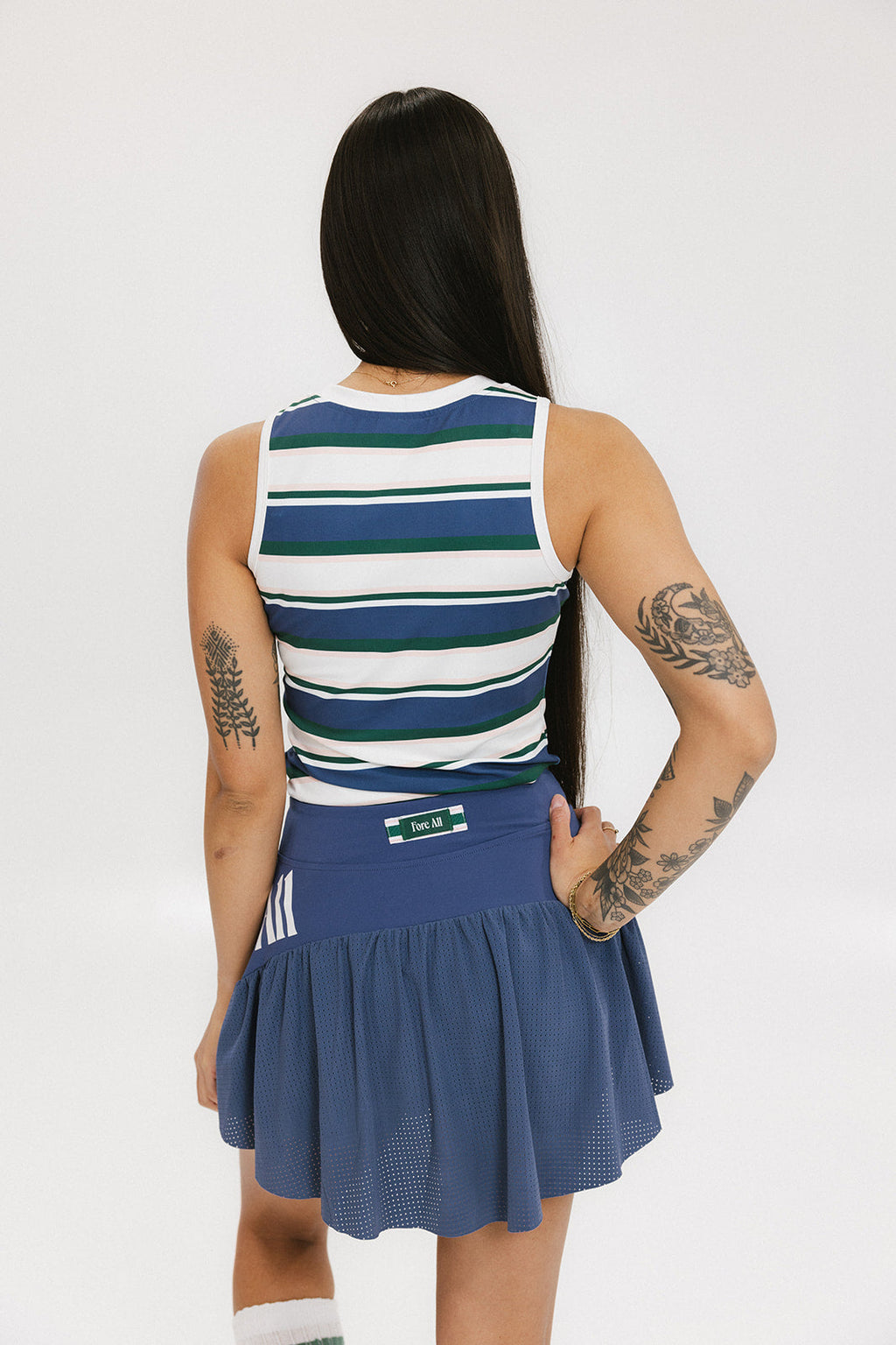 A woman wearing a sleeveless tank top with a striped pattern in blue and white colors, paired with a solid blue skirt.