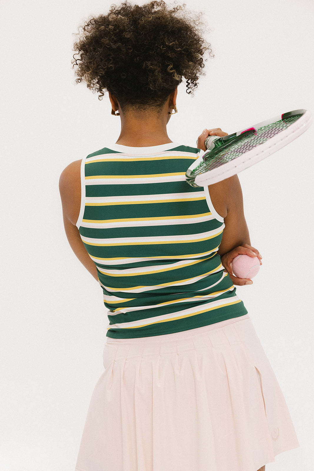 A person viewed from behind wearing a sleeveless mustard yellow and green striped tank top with white skirt.