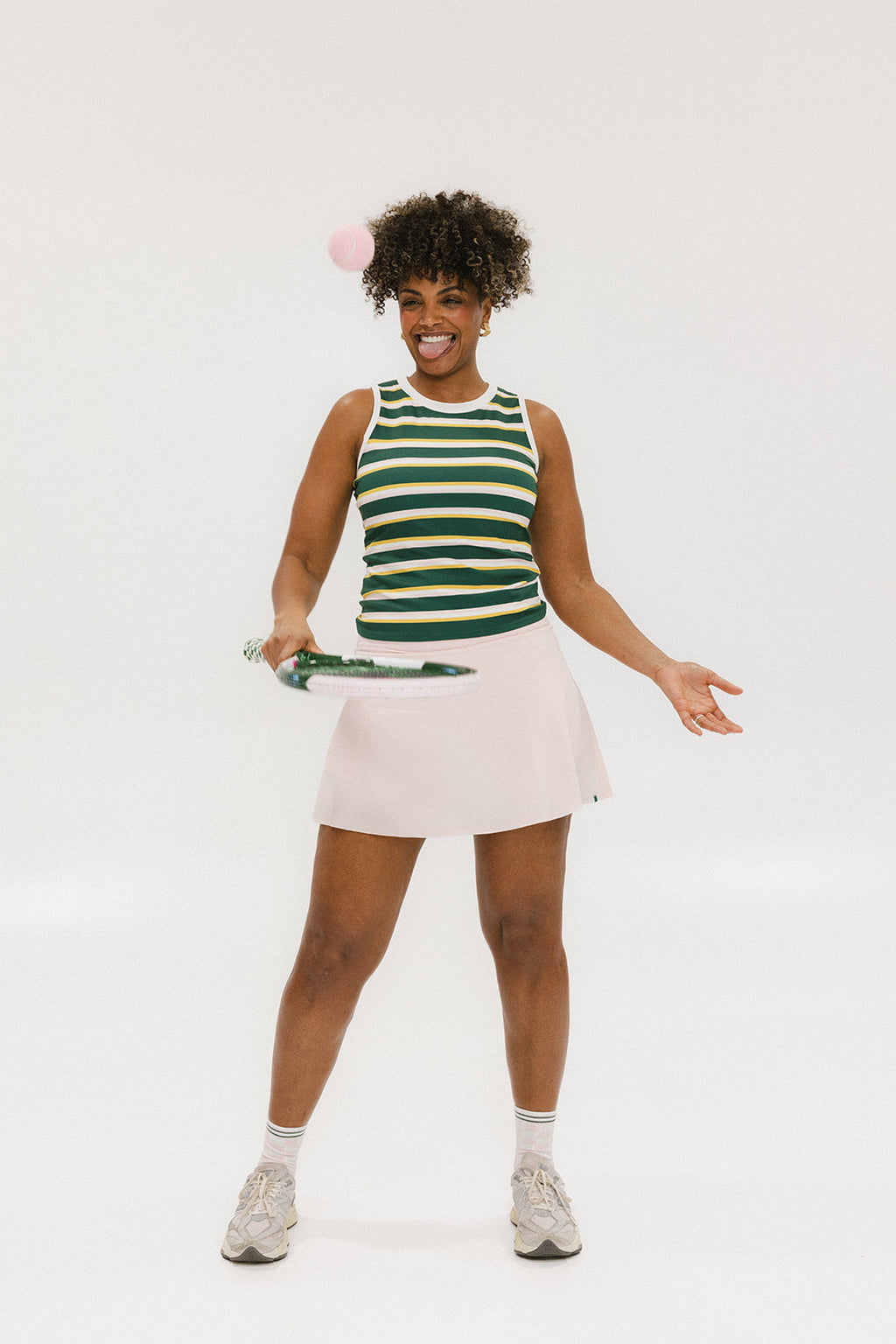 A woman smiling and wearing a sleeveless tank top with green and yellow stripes and a solid white neckline and armholes.