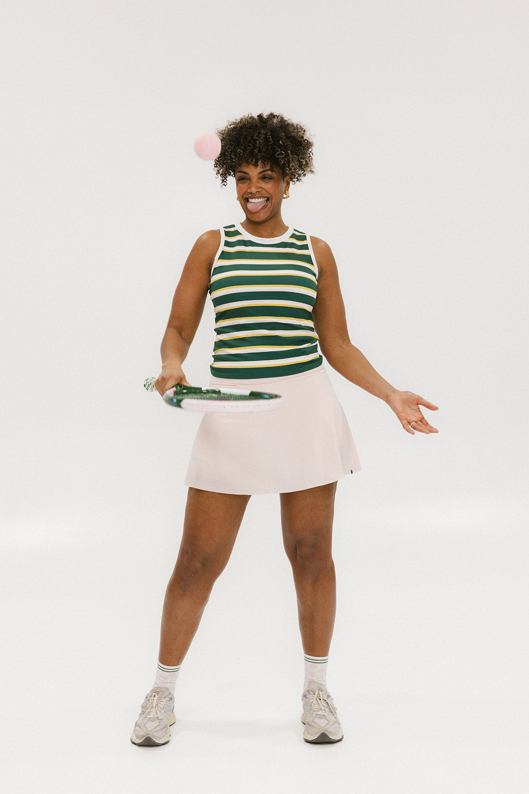 A woman smiling and wearing a sleeveless tank top with green and yellow stripes and a solid white neckline and armholes.