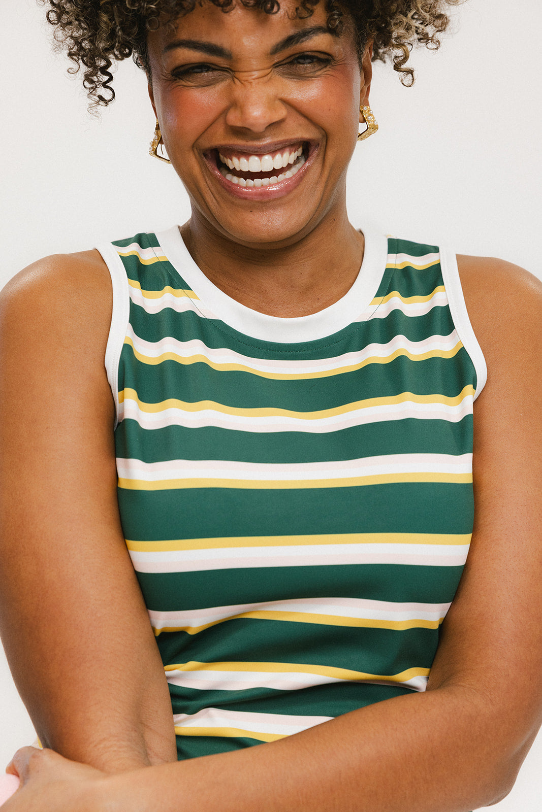 A woman smiling and wearing a sleeveless tank top with green and yellow stripes and a solid white neckline and armholes.