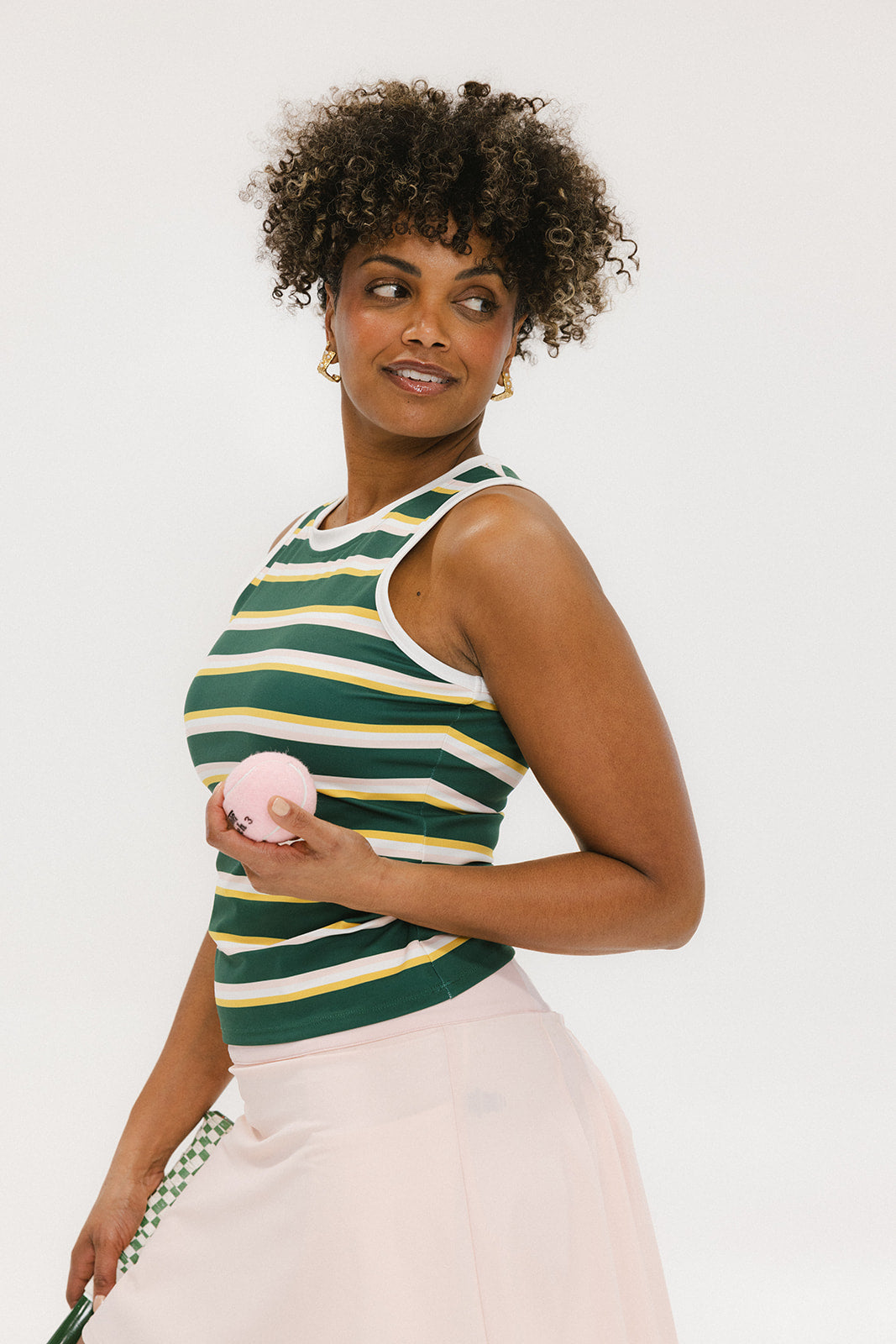A woman smiling and wearing a sleeveless tank top with green and yellow stripes and a solid white neckline and armholes.