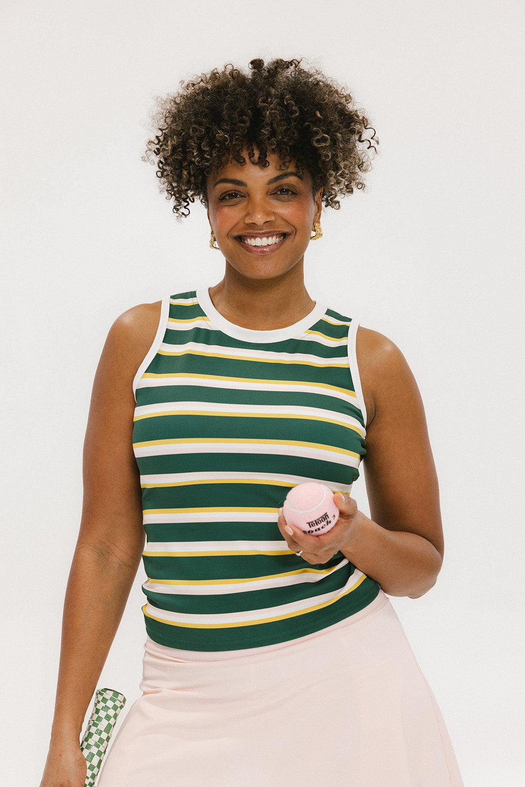 A woman smiling and wearing a sleeveless tank top with green and yellow stripes and a solid white neckline and armholes.