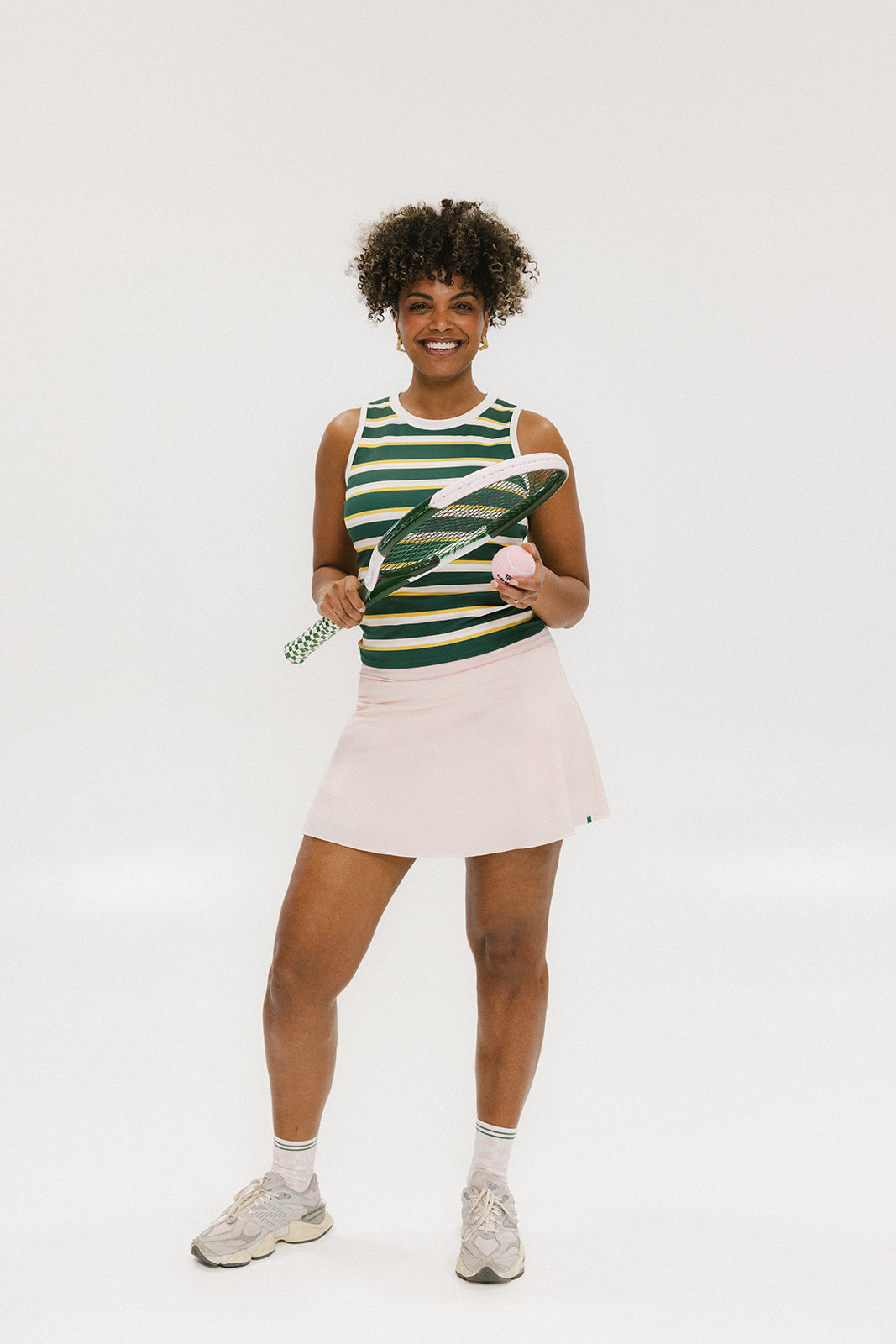 A woman smiling and wearing a sleeveless tank top with green and yellow stripes and a solid white neckline and armholes.
